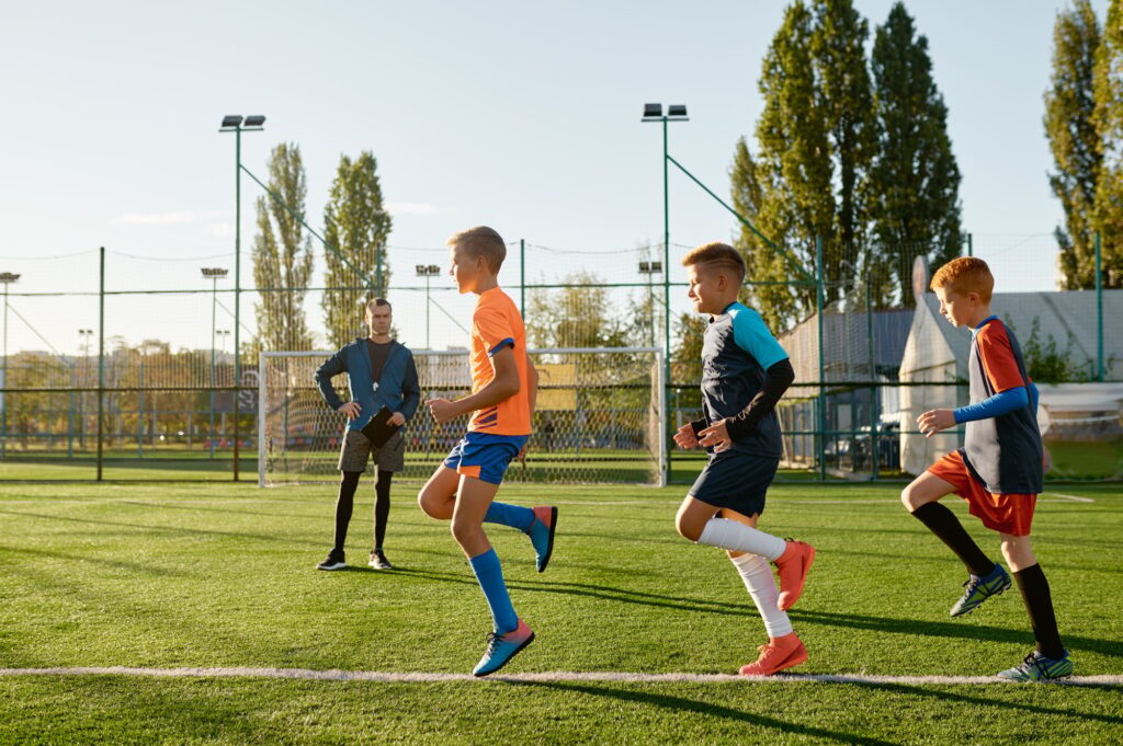 Kids practicing soccer on grass field under football coach control - Olly On The Ball Kids practicing soccer on grass field under football coach control