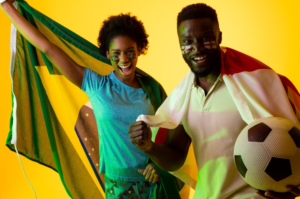 Image of african american soccer fan couple with flags of brazil and england in yellow lightning