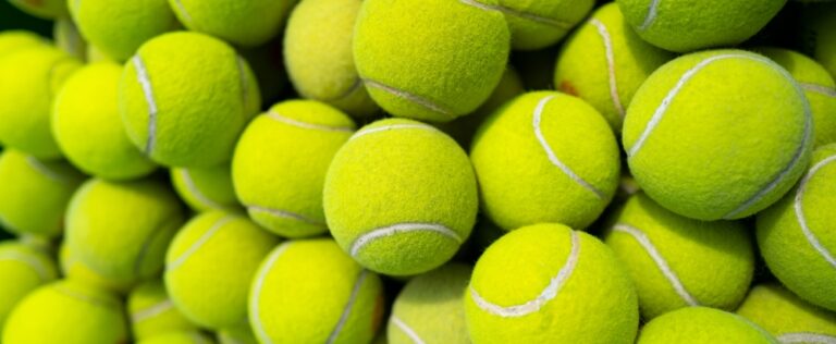 Dozens of bright yellow-green tennis balls are stacked closely together, filling the frame.
