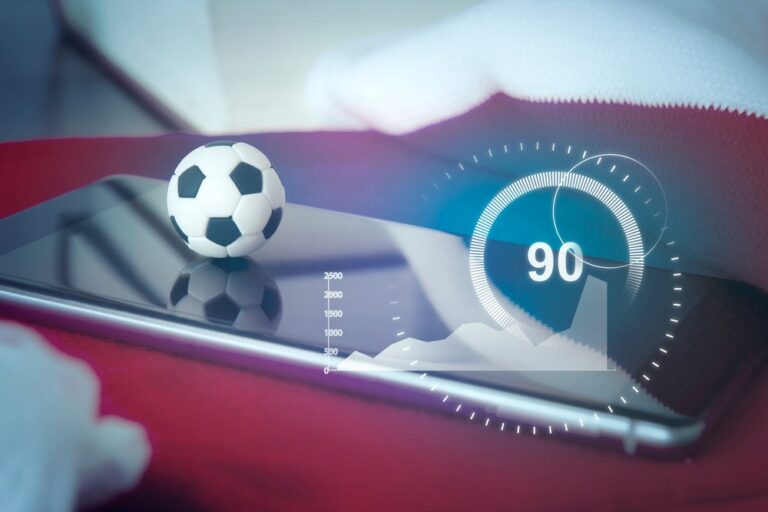 A small soccer ball rests on a smartphone displaying a glowing sports statistics graphic.