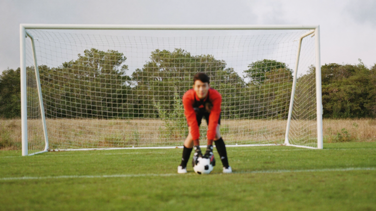 Young goalkeeper in a ready stance in front of goal during youth keeper training