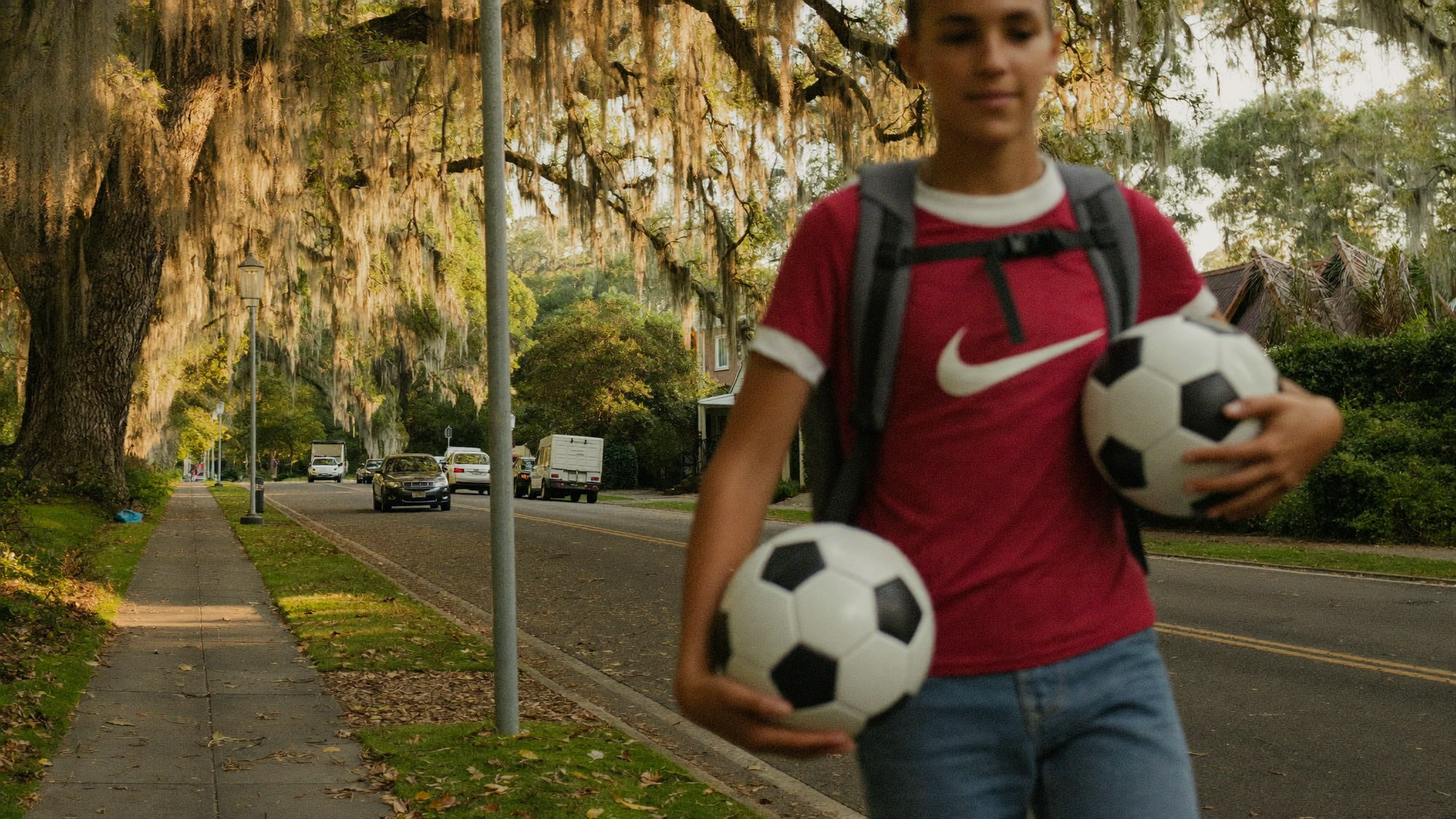 Teenage student walking home with a backpack and soccer ball along a Charleston street lined with live oaks