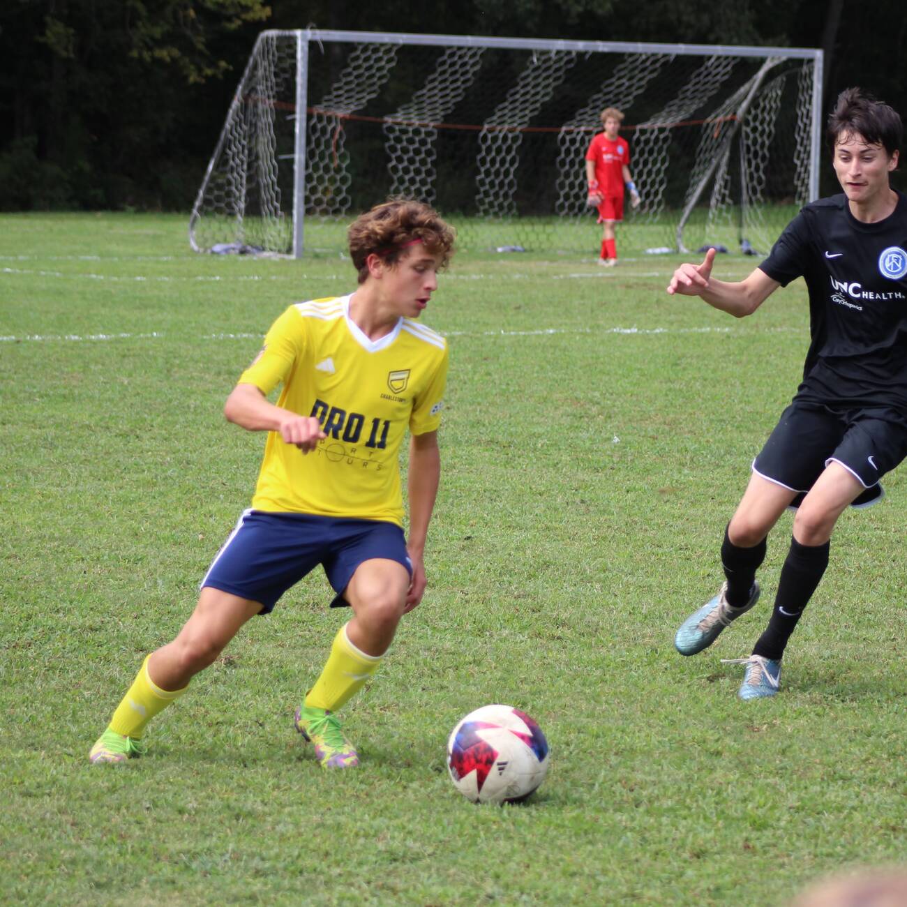 Youth player in yellow shielding the ball from a defender in black