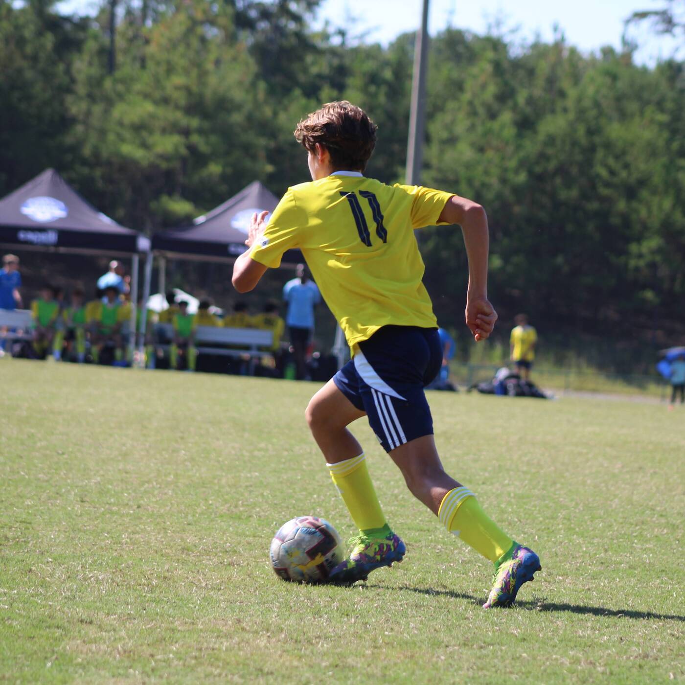 Youth soccer player dribbling in a yellow number 11 kit during a match