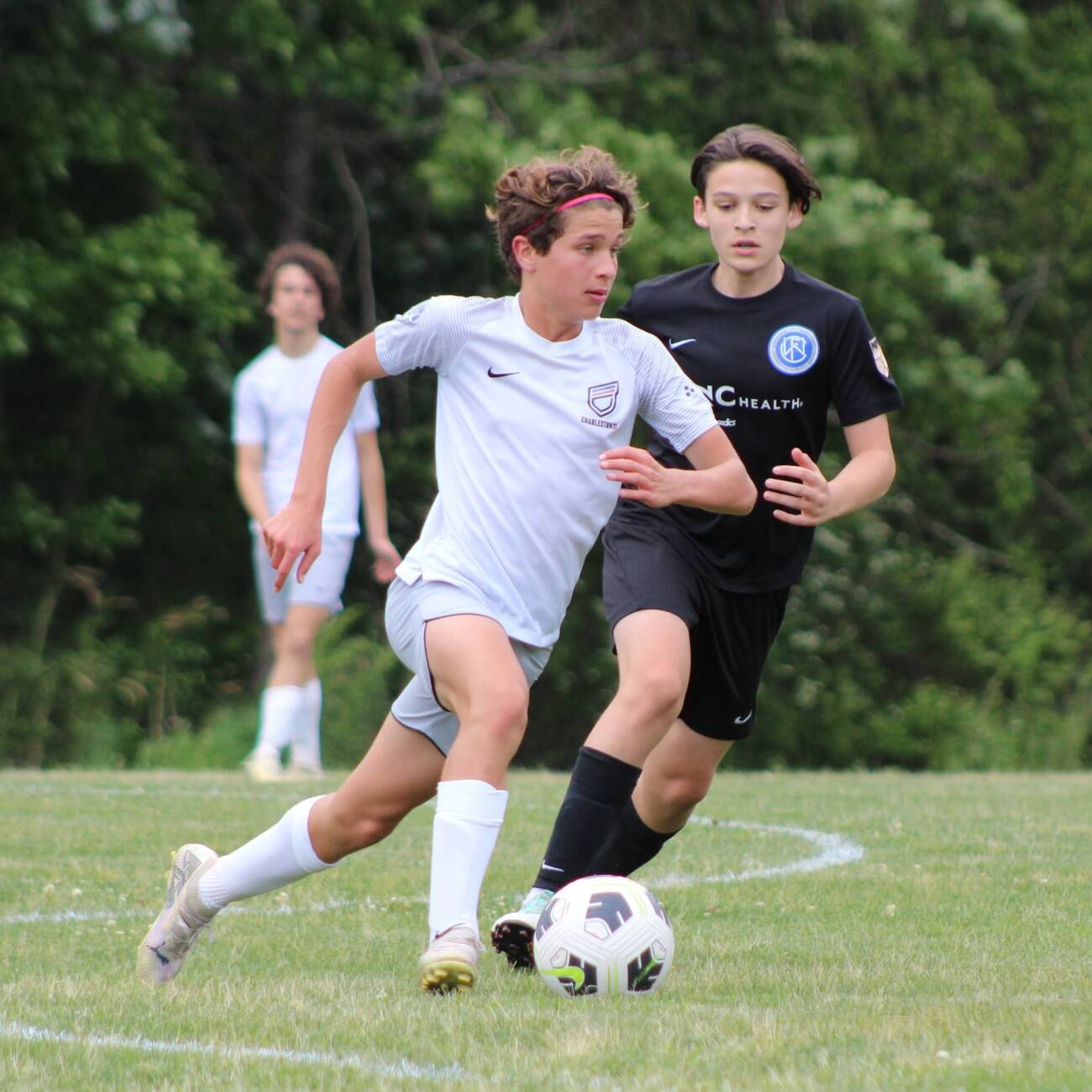 Youth player in a white kit dribbling past a defender